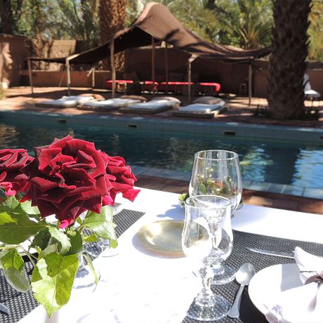 Blick auf einen gedeckten Tisch mit einer Rose am Pool der Oasenlodge Dar Qamar