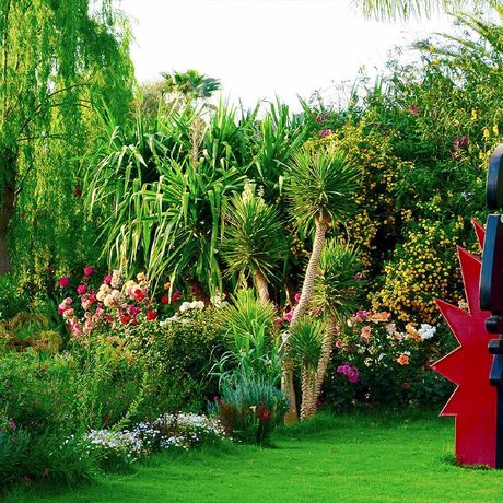 Blick auf eine Kunstskulptur auf einer Wiese neben bunten Pflanzen im Andre Heller Garten