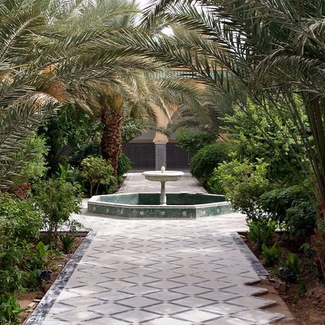 Blick auf einen Springbrunnen zwischen Baeumen und Pflanzen in einem Garten in Marokko
