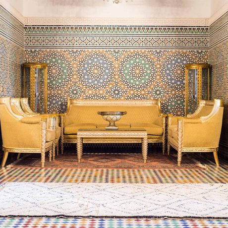Blick auf ein Sofa und Sessel vor einer verzierten Wand in einem Gebaeude in Marrakesch