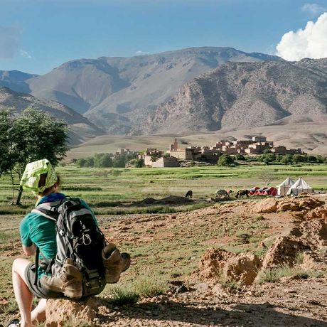Blick auf eine sitzende Person auf einer Wiese vor einem Dorf in Marokko