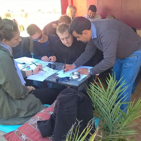 Lehrer hilft einer Gruppe an einem Tisch bei der Kalligrafie 