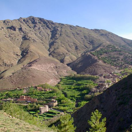 Blick auf ein gruen gelegenes Dorf am Fusse eines Berges in Marokko