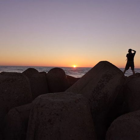 Blick auf eine Person auf Steinen beim Sonnenuntergang  am Strand des Nordatlantiks