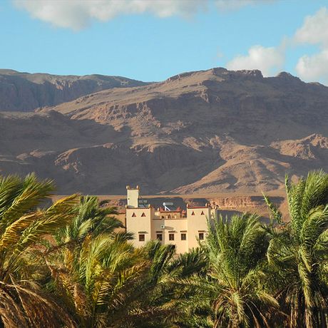 Blick auf das Kasbah-Hotel Petit Nomade zwischen Palmen und Bergen