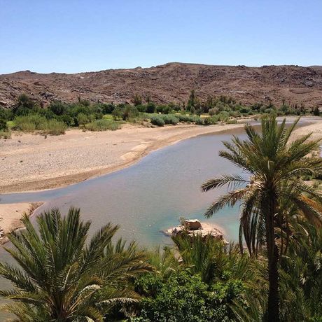 Blick auf einen Fluss, Palmen und Duenen im Tal von Sidi Flah