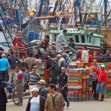 Blick auf Menschen, bunte Kisten und Schiffe im Hafen von Essaouira
