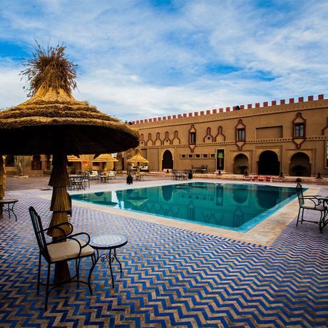 Blick auf Tische und Stuehle unter Sonnenschirmen am Pool des Kasbah-Hotels Ziz Palace