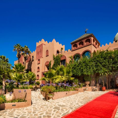 Blick auf den Eingangsbereich zwischen Palmen und Pflanzen des Kasbah-Hotels Tamadot